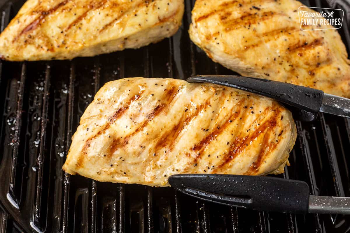 Tongs with lemon garlic grilled chicken breasts.