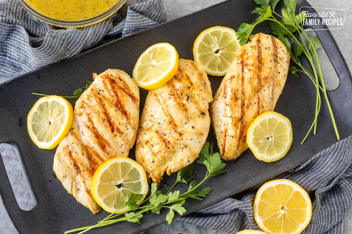 Lemon Garlic chicken breasts on a platter with bowl of marinade on the side.