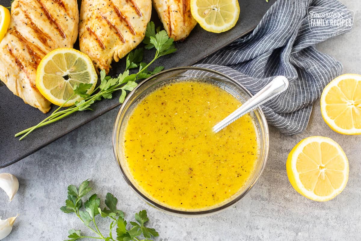 Bowl of lemon garlic chicken marinade with grilled chicken breasts on the side.