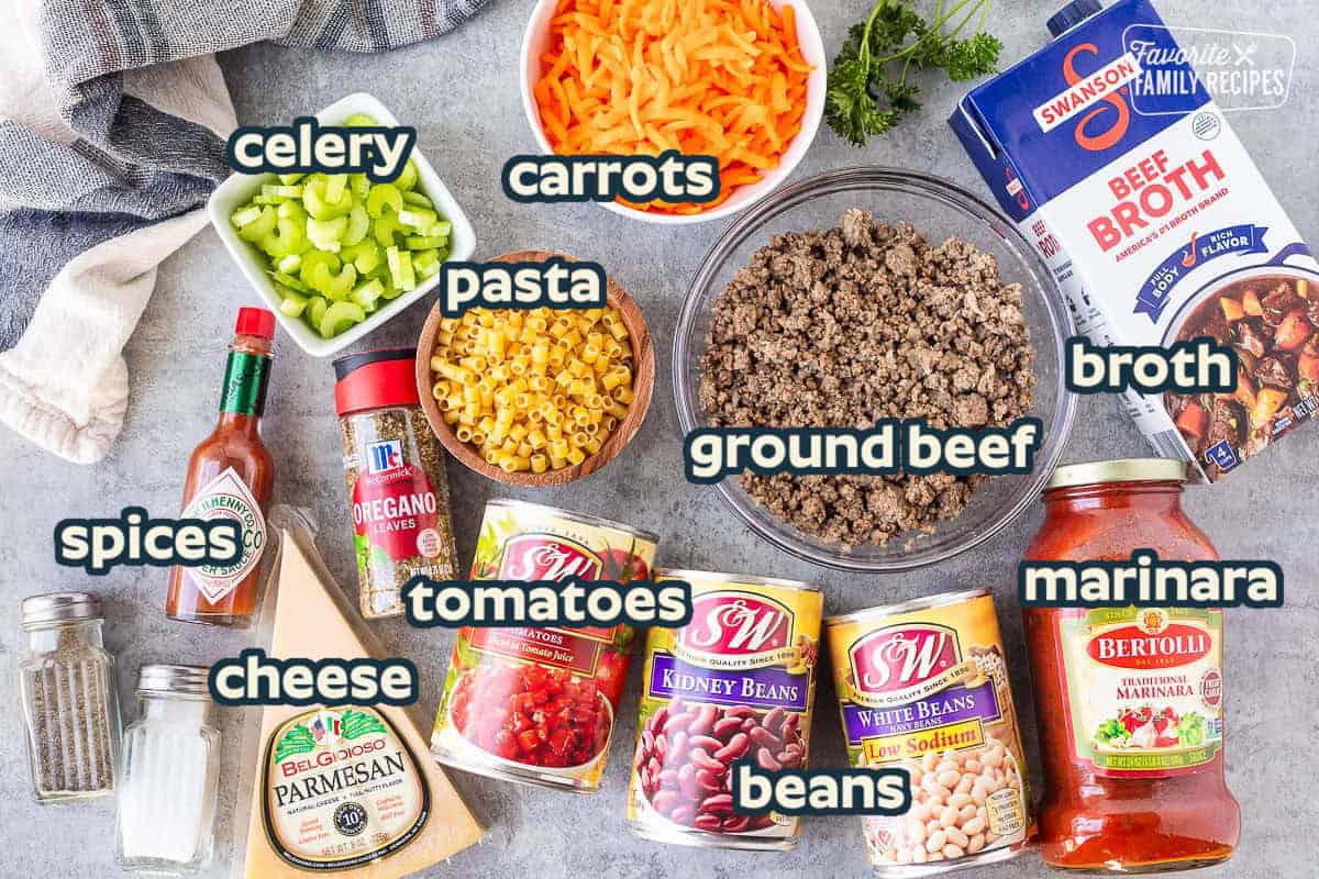 Ingredients to make Pasta e Fagioli including ground beef, beef broth, marinara sauce, white beans, kidney beans, diced tomatoes, parmesan cheese, oregano, tabasco sauce, salt, pepper, pasta, celery, shredded carrot and fresh parsley.