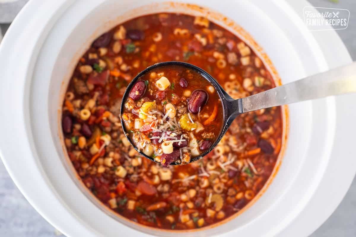 Crock pot full of pasta e fagipoli and a ladle lifting up a serving.