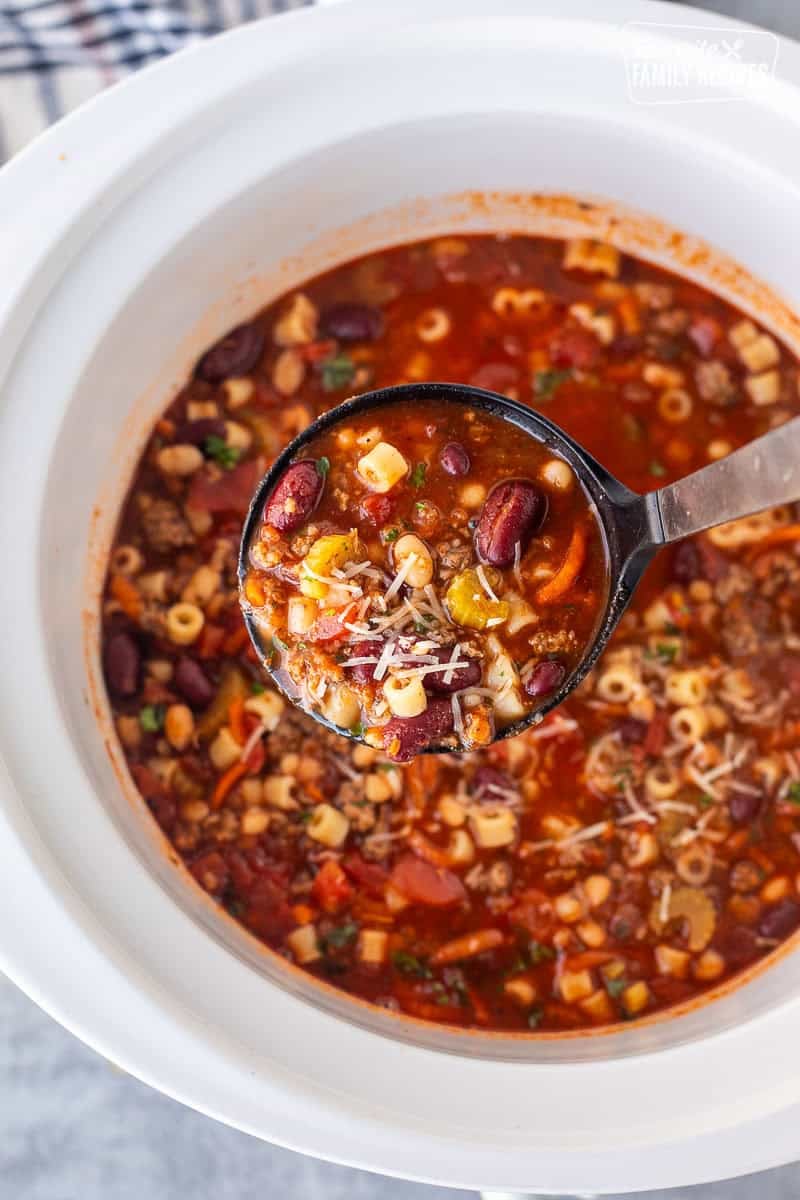 Crock pot full of pasta e fagipoli and a ladle lifting up a serving.