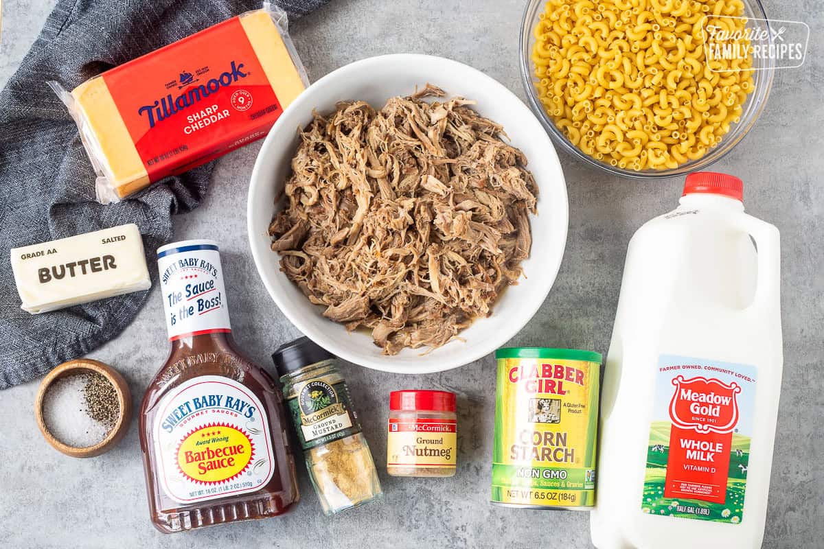 Ingredients to make pulled pork mac and cheese including macaroni noodles, sharp cheddar, cornstarch, spices, whole milk, and cooked pulled pork and barbecue sauce.
