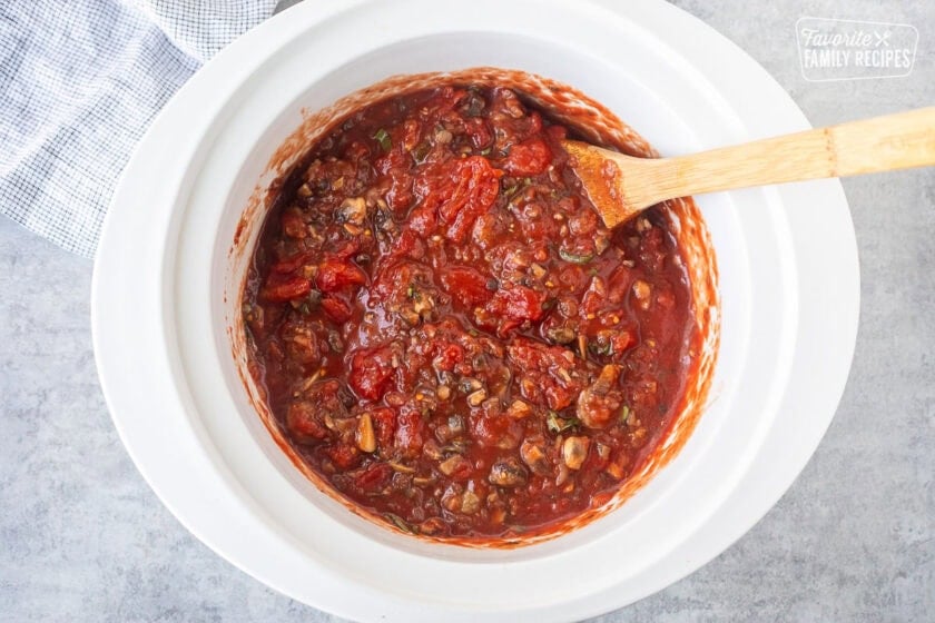 Crockpot with mixed spaghetti sauce and wooden spoon.
