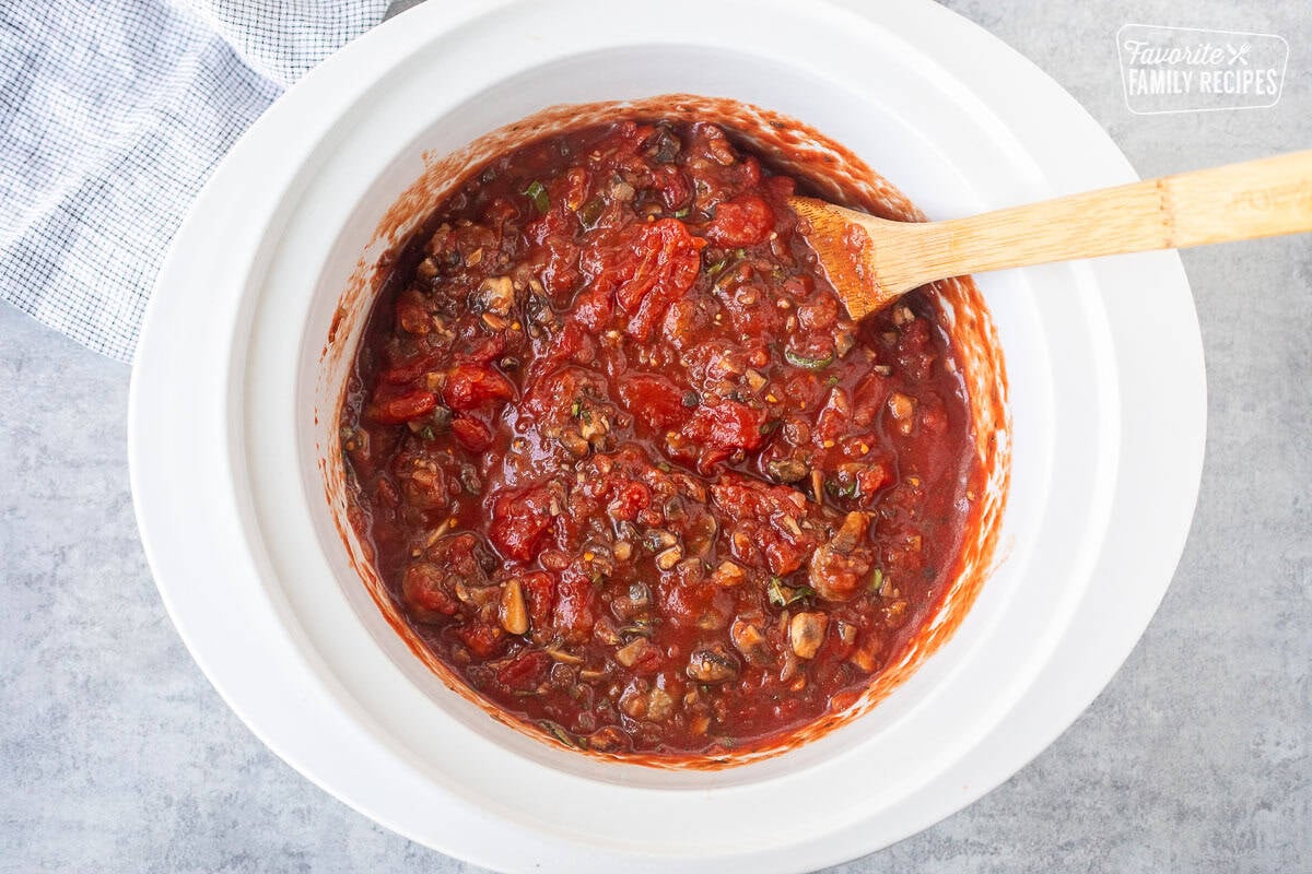 Crockpot with mixed spaghetti sauce and wooden spoon.