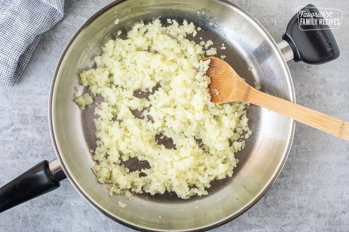 Skillet with cooked diced onions and wooden spoon.