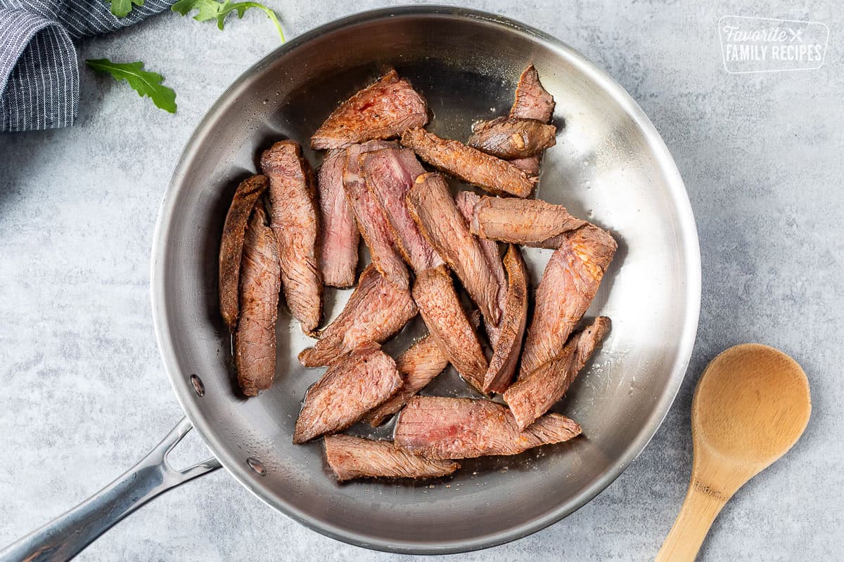 Skillet with steak heated with oil and wooden spoon on the side.