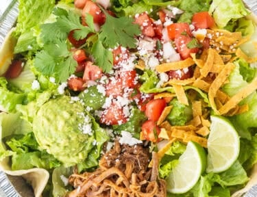 Cafe Rio Sweet Pork salad in a metal dish with lime wedges, pico de Gallo, cilantro, guacamole, cojita cheese and side of cilantro ranch dressing.