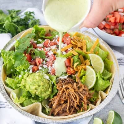Pouring Cafe Rio Creamy Tomatillo Ranch Dressing onto a Cafe Rio sweet pork salad.