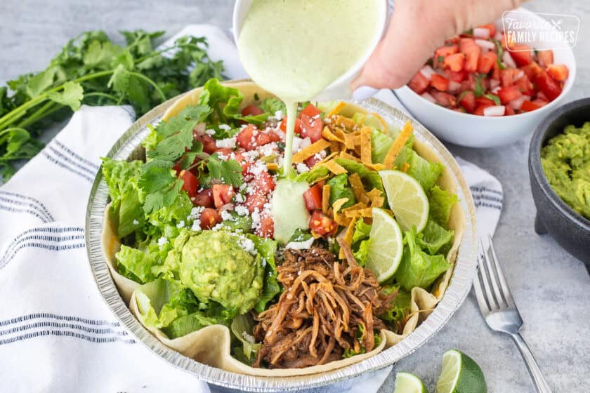 Pouring Cafe Rio Creamy Tomatillo Ranch Dressing onto a Cafe Rio sweet pork salad.