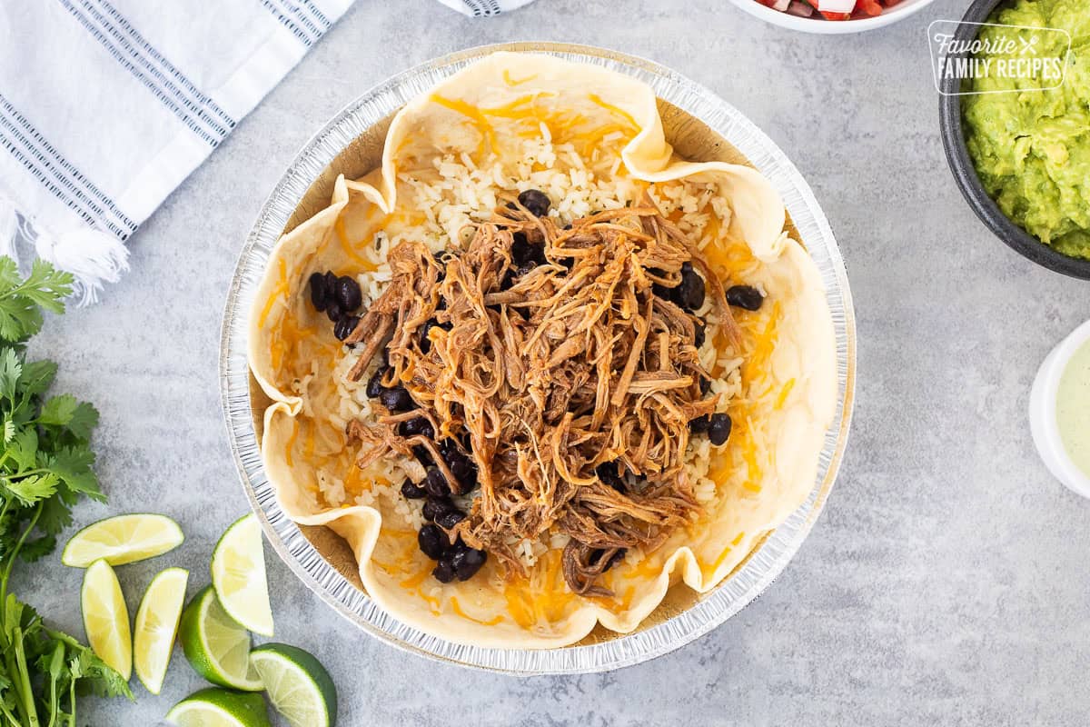 Metal dish with tortilla, melted cheese, rice, black beans and sweet pork.