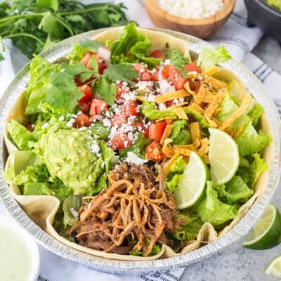 Cafe Rio Sweet Pork salad in a metal dish with lime wedges, pico de Gallo, cilantro, guacamole, cojita cheese and side of cilantro ranch dressing.