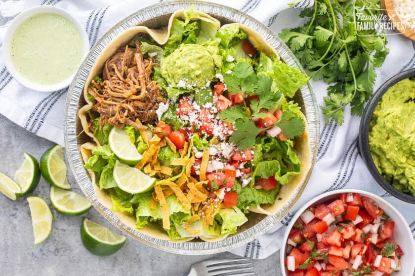 Cafe Rio Sweet Pork salad in a metal dish with lime wedges, pico de Gallo, cilantro, guacamole, cojita cheese and side of cilantro ranch dressing.