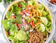 Cafe Rio Sweet Pork salad in a metal dish with lime wedges, pico de Gallo, cilantro, guacamole, cojita cheese and side of cilantro ranch dressing.