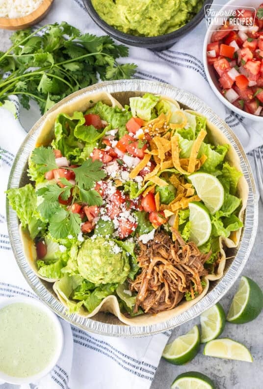 Cafe Rio Sweet Pork salad in a metal dish with lime wedges, pico de Gallo, cilantro, guacamole, cojita cheese and side of cilantro ranch dressing.