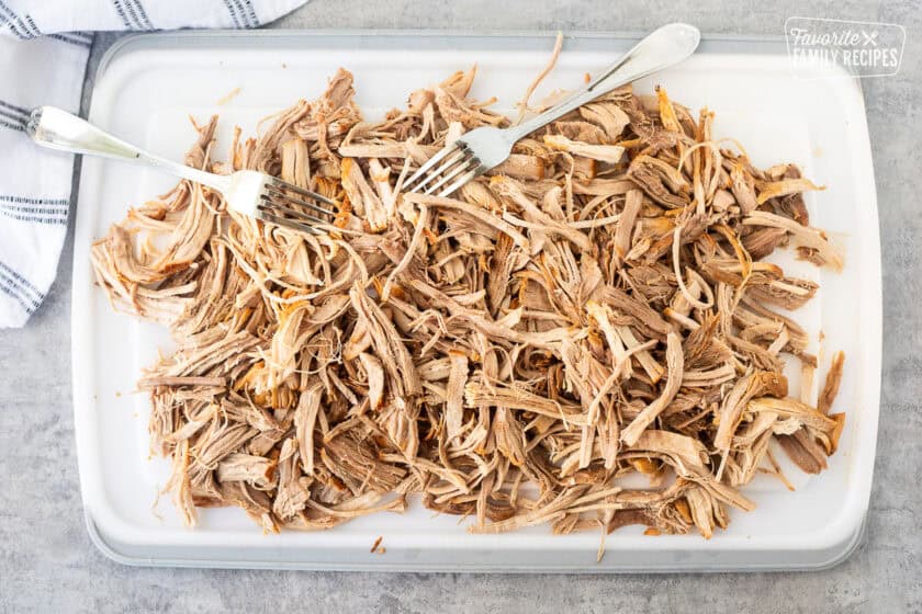 Shredding cooked pork roast with forks on a cutting board.