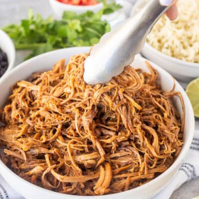 Bowl of Cafe Rio Sweet Pork with tongs. Sides of rice and black beans on the side.