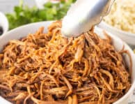 Bowl of Cafe Rio Sweet Pork with tongs. Sides of rice and black beans on the side.