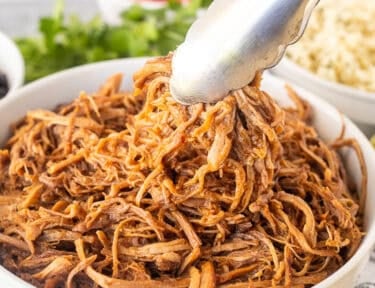 Bowl of Cafe Rio Sweet Pork with tongs. Sides of rice and black beans on the side.