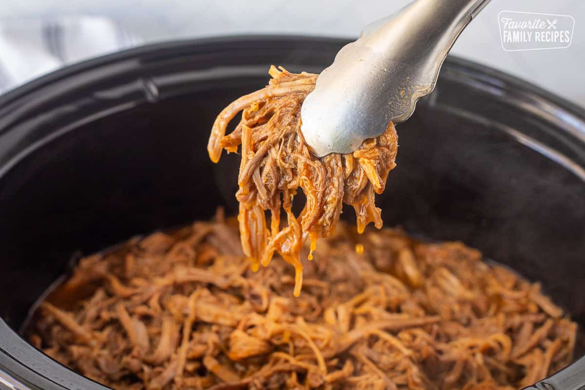 Lifting up Cafe Rio sweet pork with tongs from a crockpot.