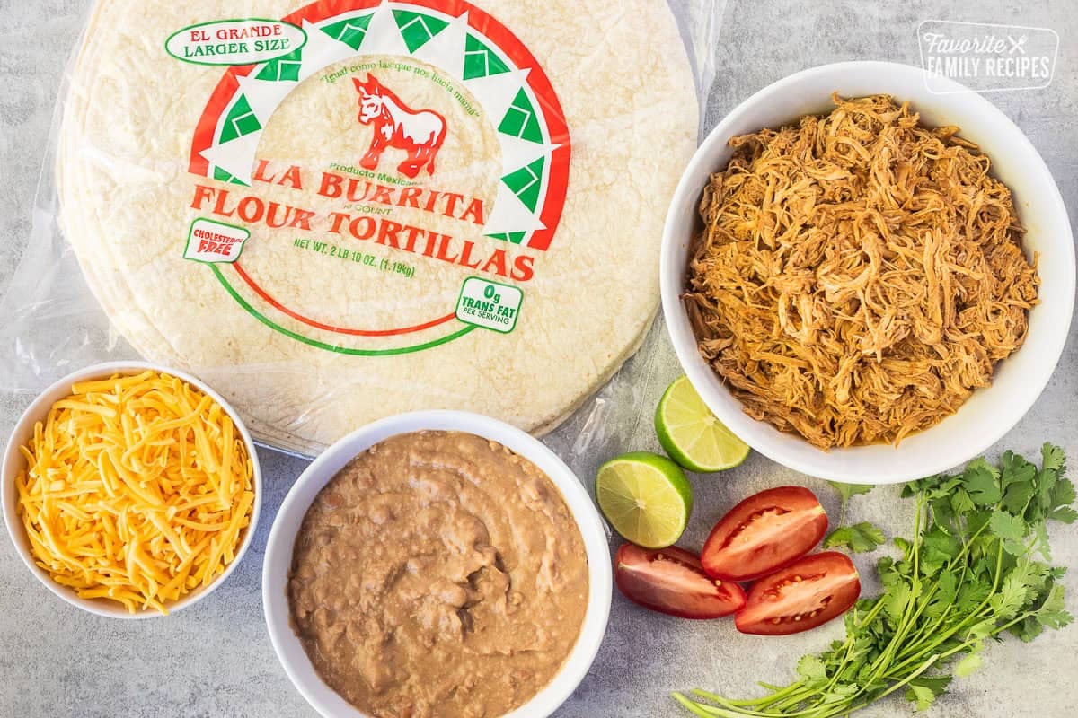 Ingredients to make Chicken Chimichangas including extra large tortillas, Mexican shredded chicken, refried beans, cheese, cilantro, lime and tomatoes.