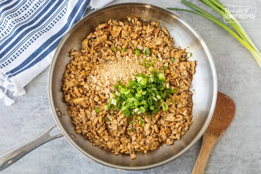 Green onion and chopped cashews mixed into velvet chicken in the skillet.