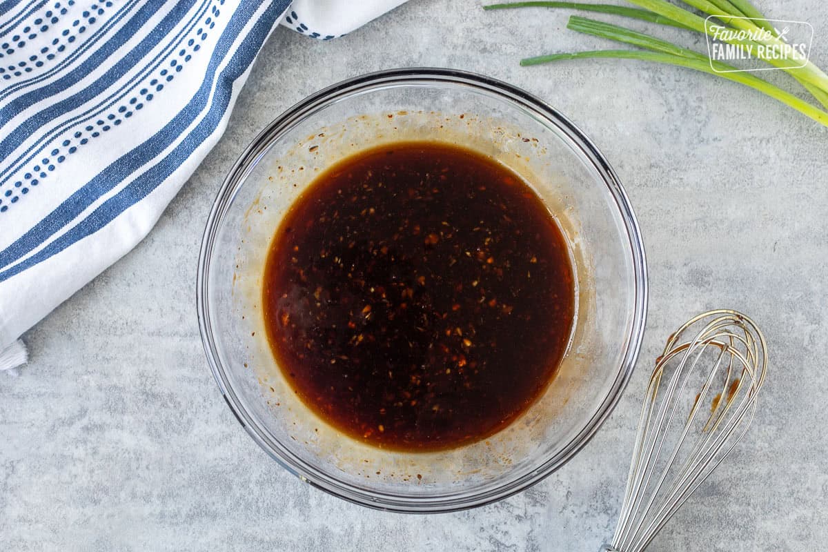Glass mixing bowl with chicken sauce and whisk on the side.