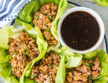 PF Changs Chicken lettuce wraps on a plate with small bowl of dipping sauce on the side.