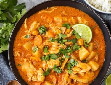 Bowl of chicken massaman curry garnished with cilantro and served with rice on the side.