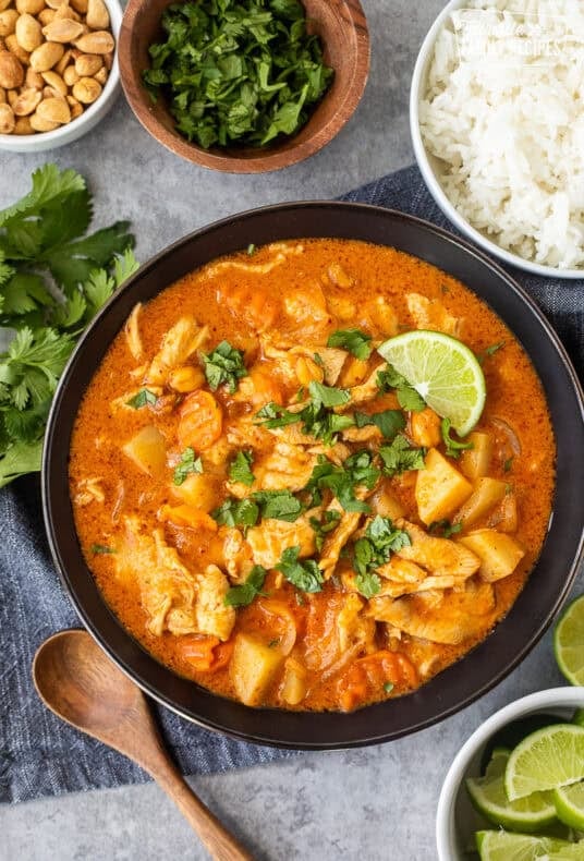 Bowl of chicken massaman curry garnished with cilantro and served with rice on the side.