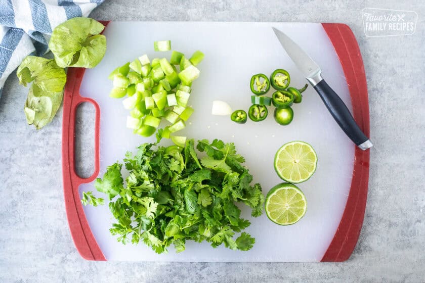 Cutting board with chopped and peeled tomatillos, jalapeño, garlic and lime.