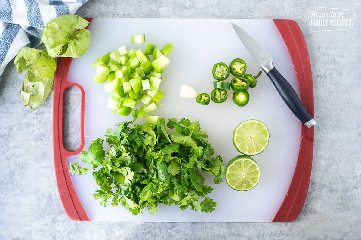 Cutting board with chopped and peeled tomatillos, jalapeño, garlic and lime.