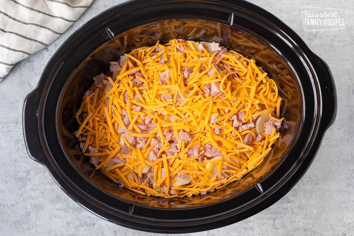 Crockpot with sliced potatoes, onion, cheddar cheese and ham layers.