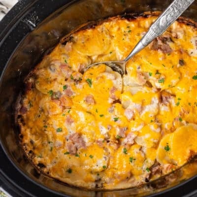 Spoon scooping ham and scalloped potatoes from a crockpot.