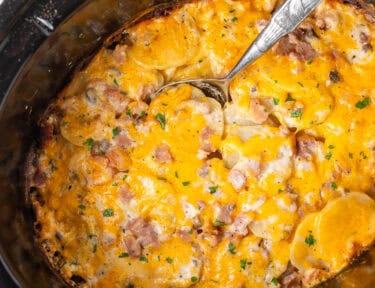 Spoon scooping ham and scalloped potatoes from a crockpot.