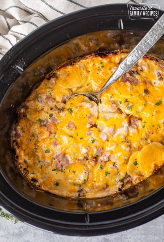 Spoon scooping ham and scalloped potatoes from a crockpot.