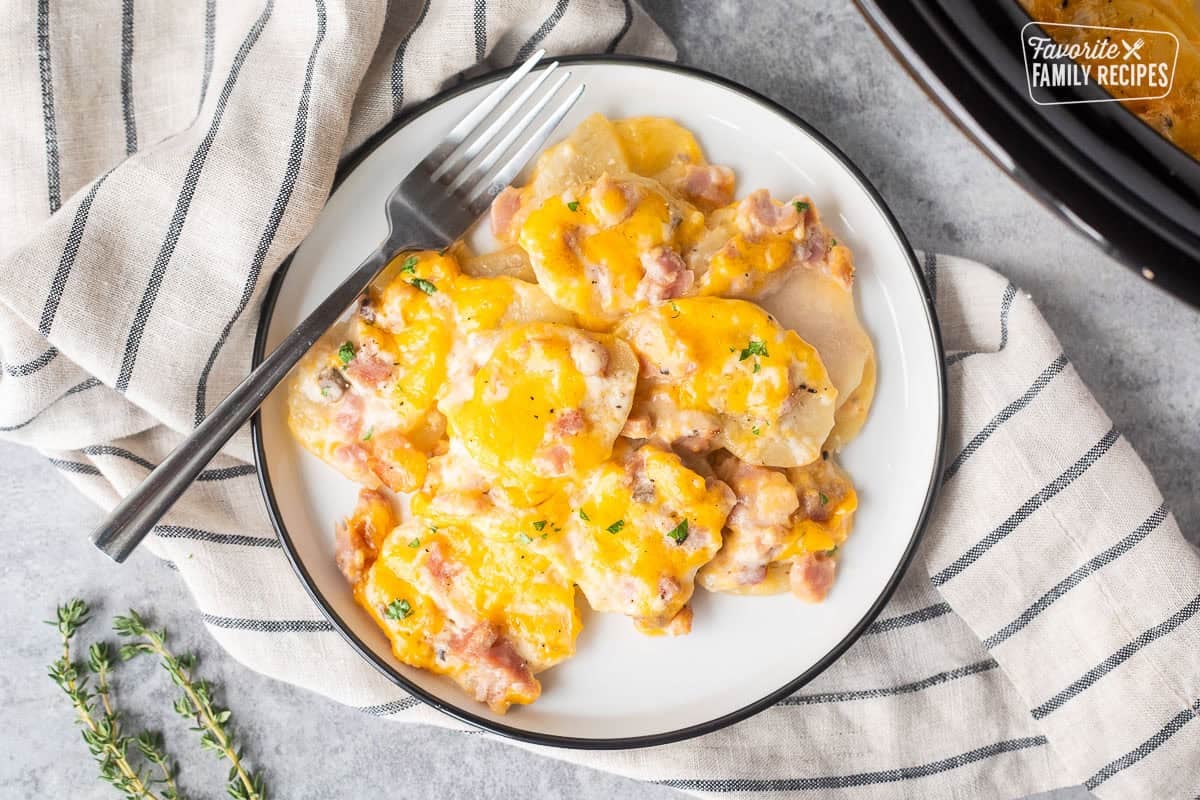 Plate with crockpot ham and scalloped potatoes with a fork.