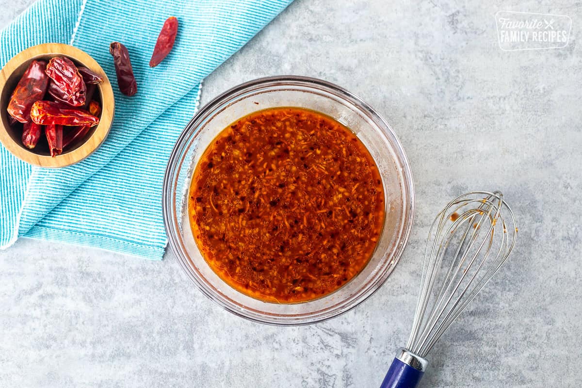 Small glass bowl of kung pao chicken marinade and whisk on the side.