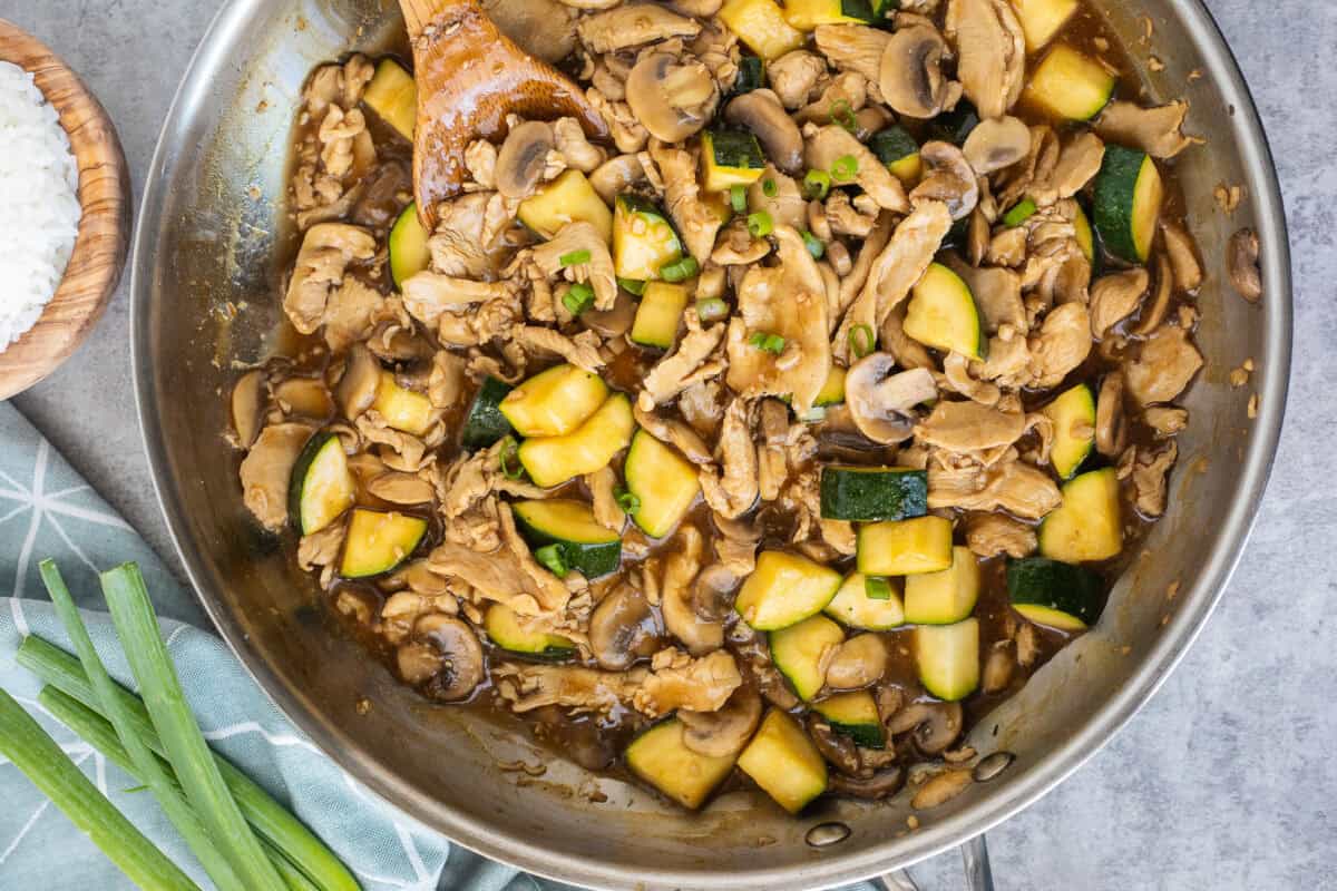 Skillet of mushroom zucchini chicken with a wooden spoon.