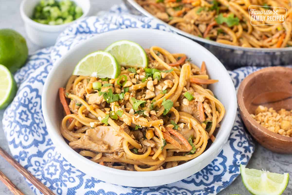 Bowl of Thai Peanut noodles topped with cilantro, peanut, lime wedges and green onion.