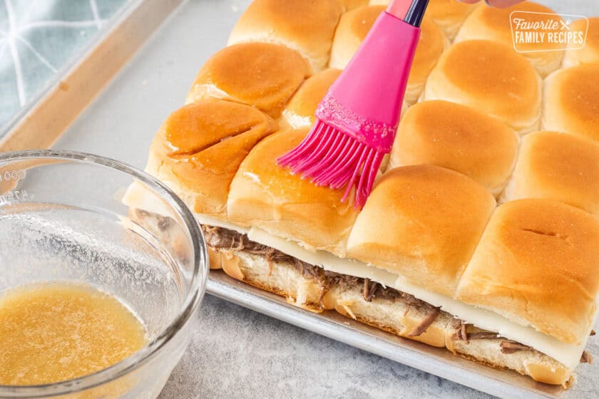 Brushing butter garlic mixture on tops of roast beef sliders.