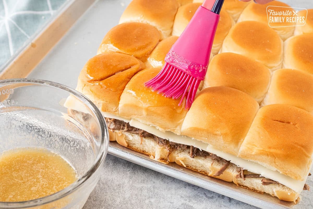 Brushing butter garlic mixture on tops of roast beef sliders.