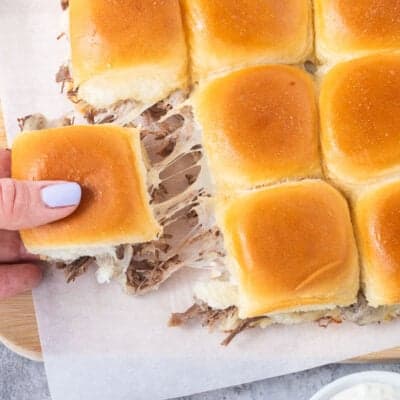 Roast beef slider being pulled apart with melted cheese stretching between the connected sliders.