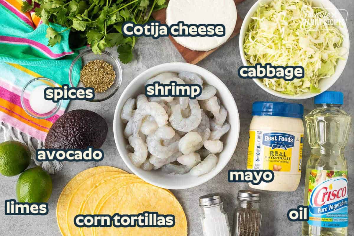 Ingredients to make shrimp tacos including shrimp, cabbage, cojita cheese, mayonnaise, corn tortillas, avocado, limes, oregano, sugar, cilantro, oil, salt and pepper.