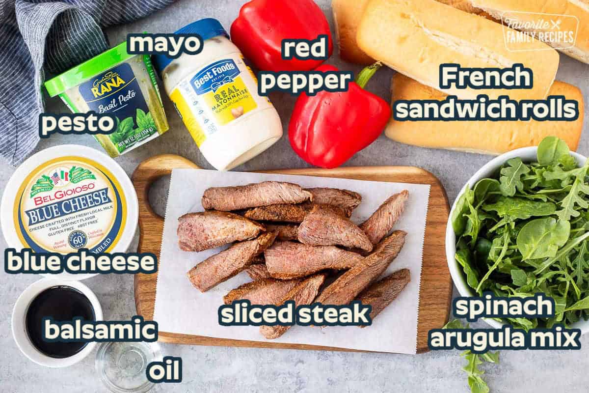Ingredients to make Steak sandwich including French rolls, arugula and spinach mix, red peppers, mayo, pesto, steak, blue cheese, balsamic vinegar and oil.