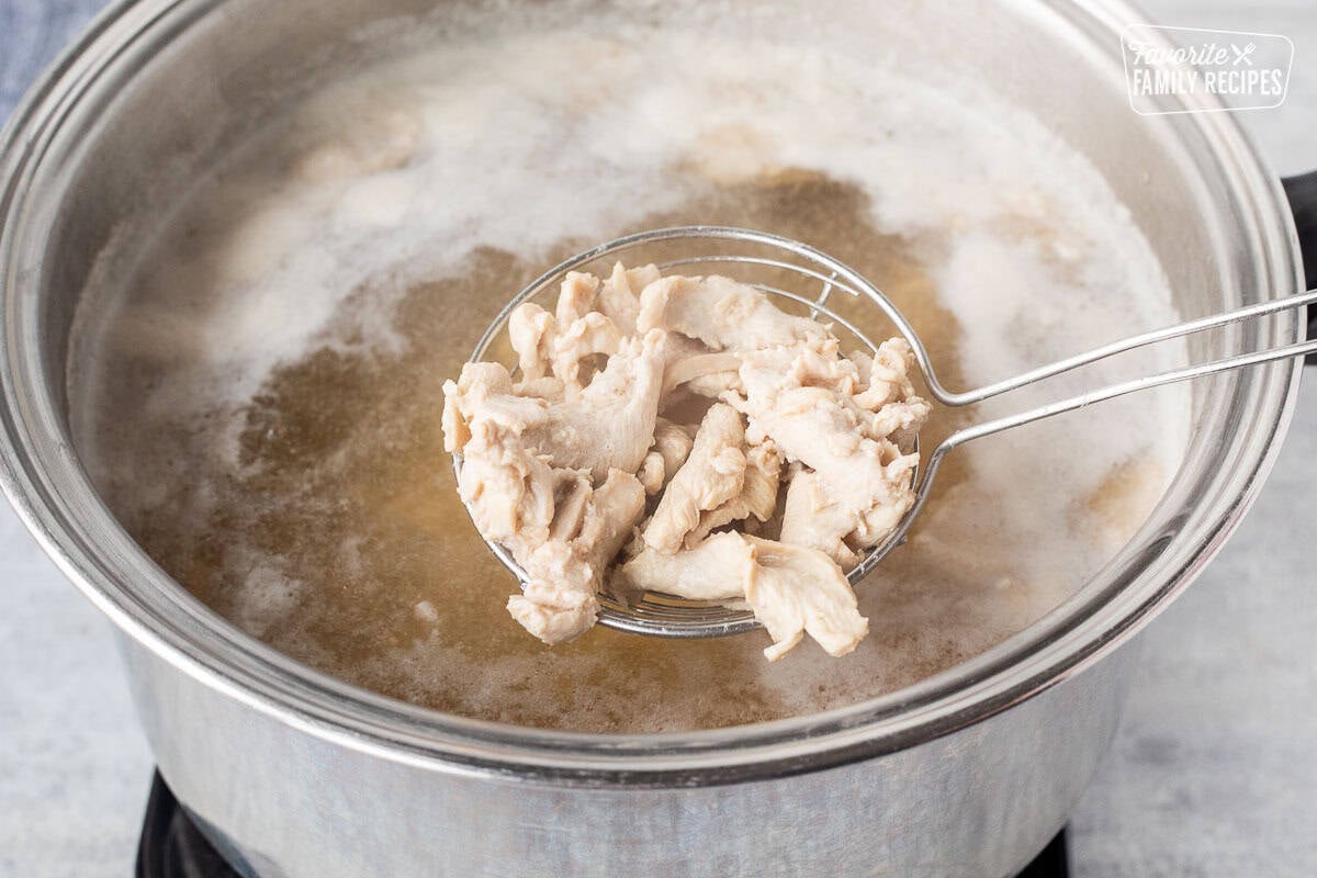 Using slotted spoon to lift cooked chicken out of the boiling pot.