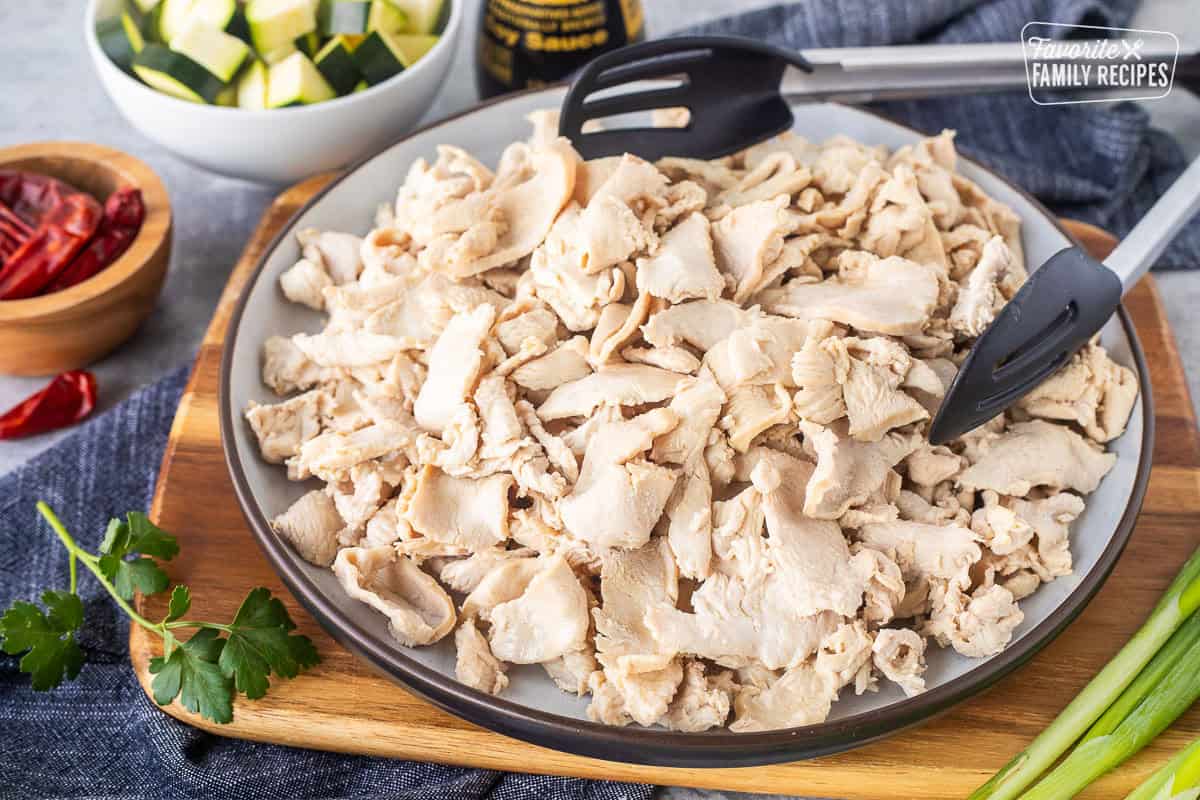Plate of cooked velvet chicken with tongs.