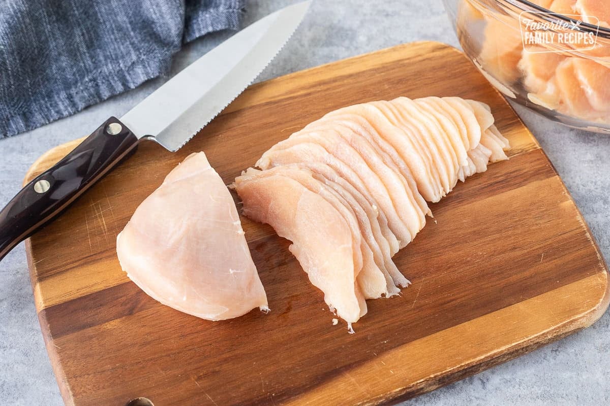 Slicing frozen chicken super thin with a sharp knife on a cutting board.