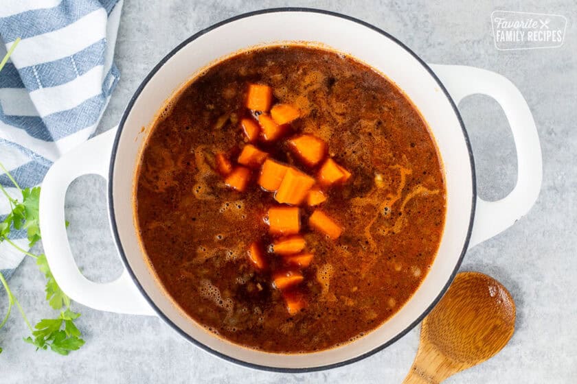 Adding cut carrots to the dutch oven with beef and broth.