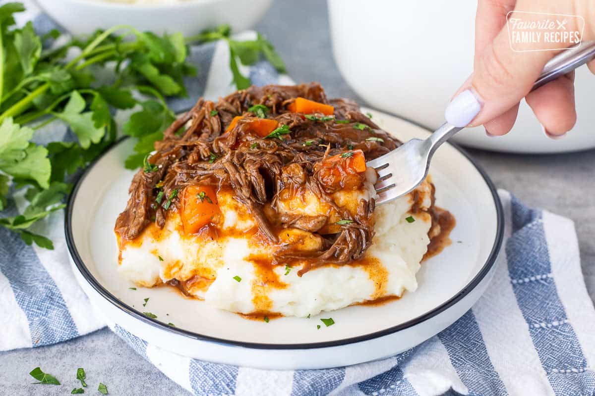 Plate of beef goulash over mashed potatoes with a fork pulling out a bite.
